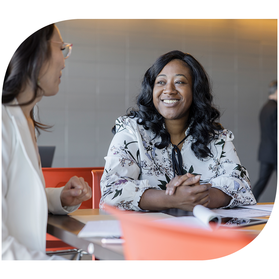 Two smiling women in a conversation at a table with notepads and documents